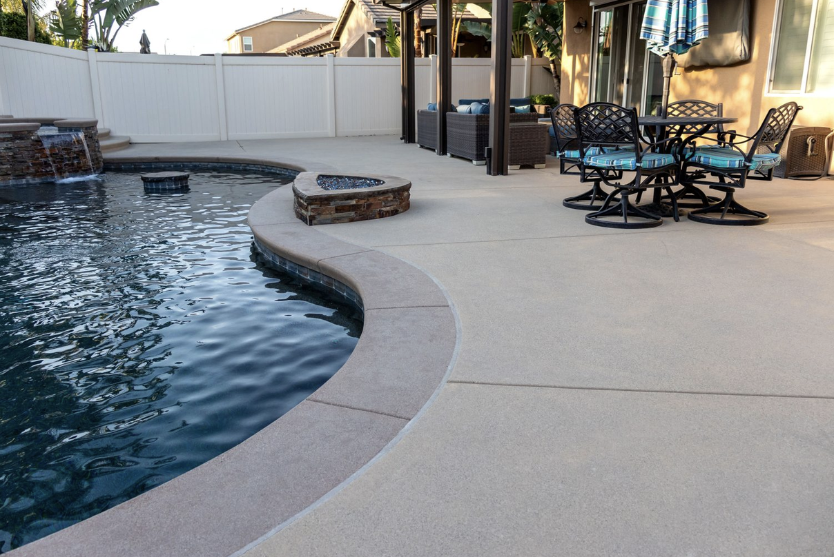 Curved concrete pool deck with a built-in fire pit seating area